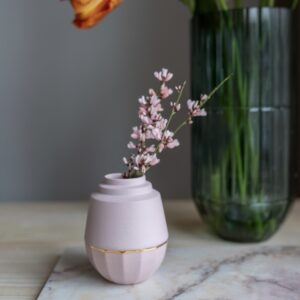 Klein roze vaasje gemaakt van porselein. Het vaasje heeft een strakke vormgeving. In het vaasje zit een klein takje met bloemetjes