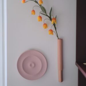 ronde wandvaas. Gemaakt van porselein. uitgevoerd in een matte roze kleur. Daarnaast hangt een langwerpig wandvaasje in hetzelfde materiaal.