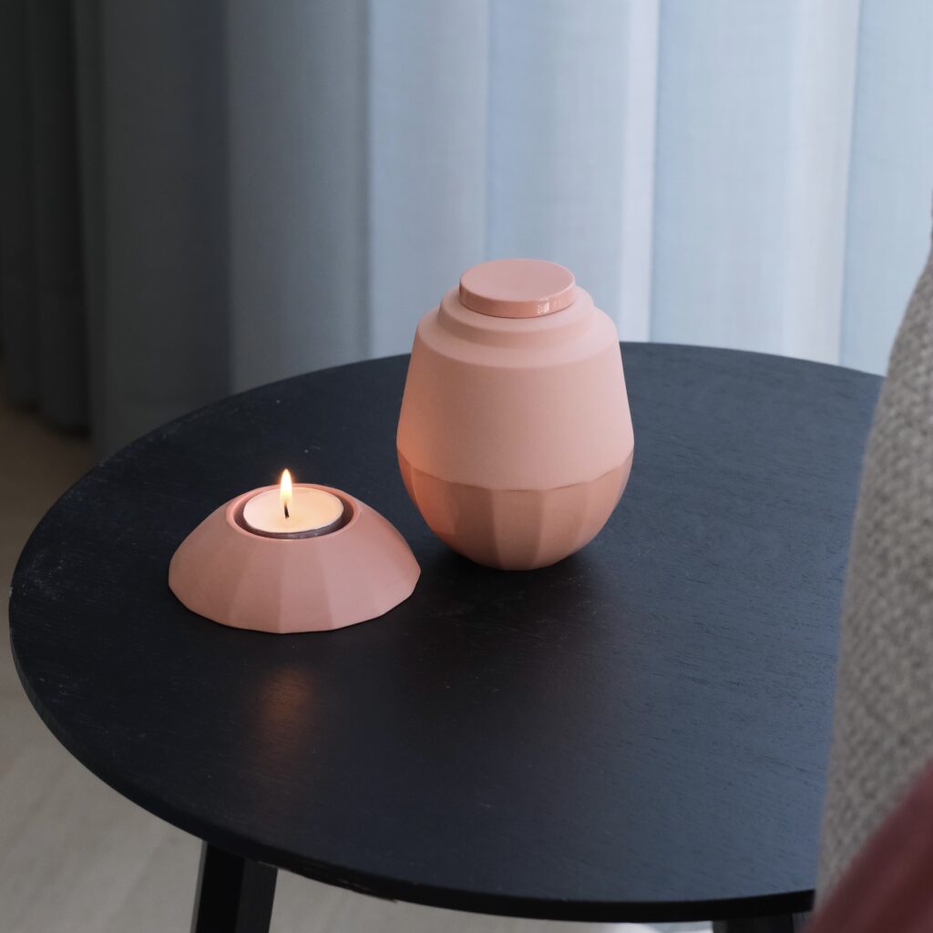 klein handgemaakt urntje met daarnaast een waxinelichthouder in dezelfde kleur. Het setje staat op een zwart tafeltje.